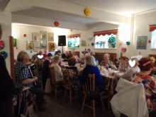 Seniorzy siedzący przy stole śpiewający do akompaniamentu akordeonisty