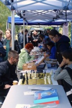 Mieszkańcy gromadzą się przy stołach z atrakcjami - na pierwszym planie szachy - dalej stoiska tematyczne