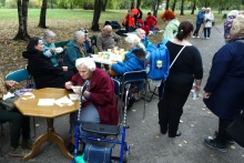 Mieszkańcy siedzą przy stołach na wolnym powietrzu rozmawiają i spożywają posiłek