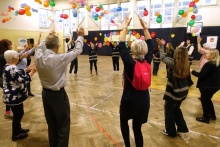 Seniorzy tańczą z młodzieżą unosząc ręce w górę