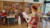 Seniorka czyta wiersz w sali udekorowanej pracami plastycznymi
