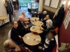 Grupa seniorów z ośrodka wspracia siedzi przy stołach i piję kawę